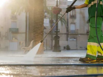 An unrecognizable worker uses a high-pressure water cleaner to remove dirt in the street.