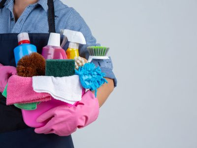Young girl is holding cleaning product, gloves and rags in the basin on white background